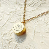 Gold necklace with a round pendant featuring a bear design on a textured beige background