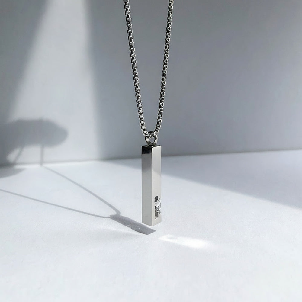 Silver necklace with a rectangular pendant on a white surface with soft shadows