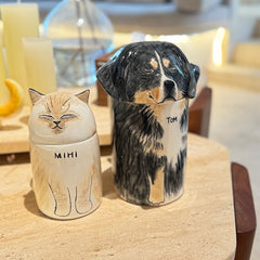 Two ceramic jars, one with a cat design labeled 'MIHI' and the other with a dog design labeled 'TOM', on a wooden surface.