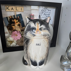 Cat-shaped jar with 'KALI' on a shelf next to a framed photo