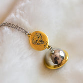 Gold pendant necklace with a round charm featuring a bear and engraved text on a white fabric background.