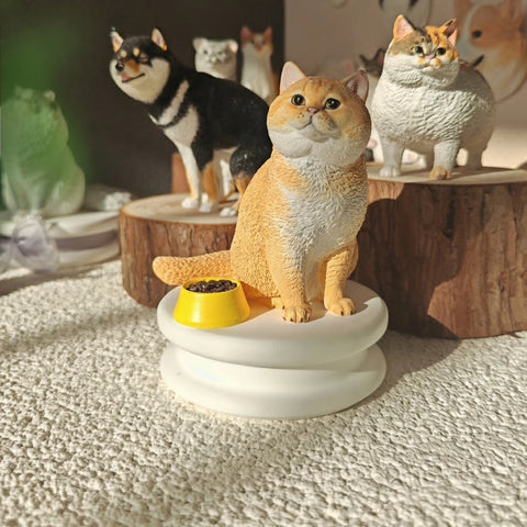 Cat figurine with a bowl of food on a white base, surrounded by other cat figurines.