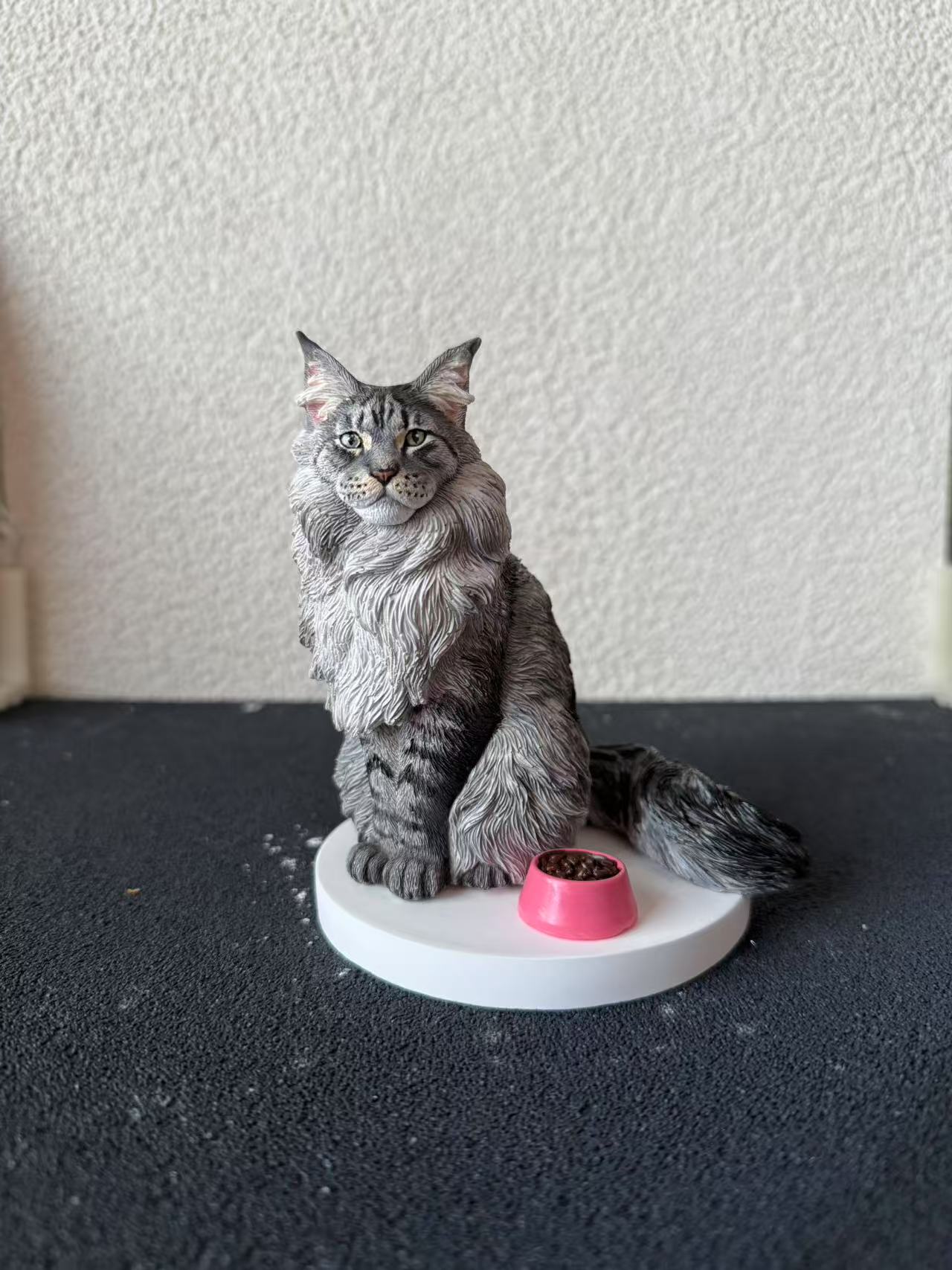 Cat figurine with a pink bowl on a white base against a textured white wall.