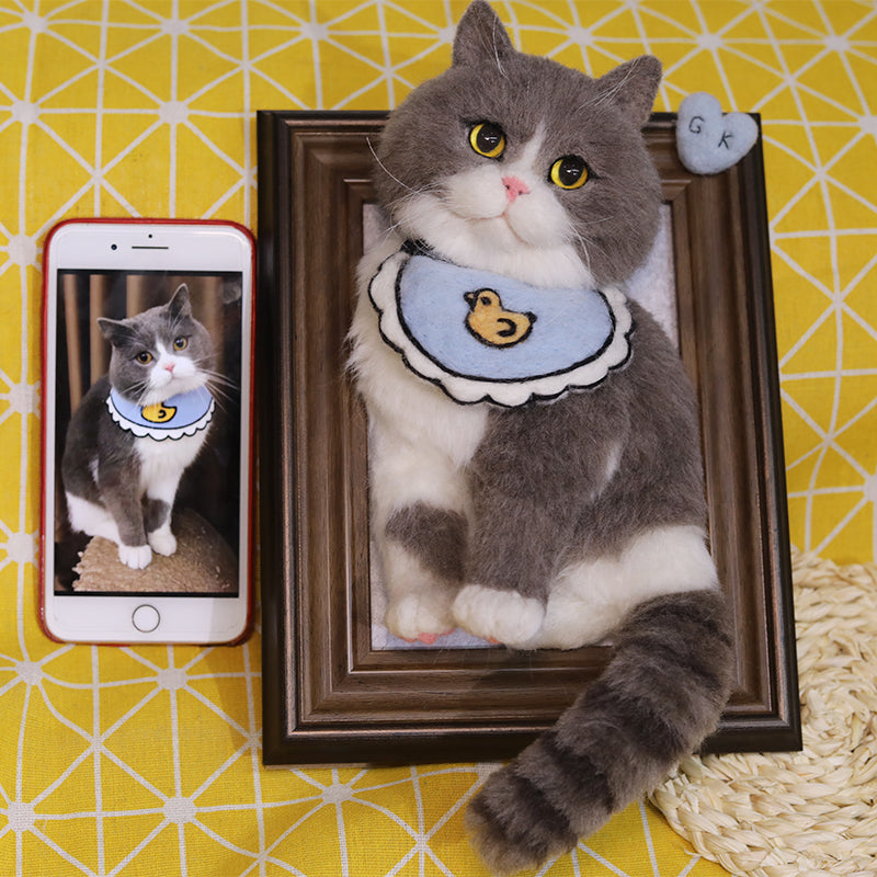Cat wearing a blue collar with a duck design, next to a smartphone showing a similar image, on a yellow and white patterned background.