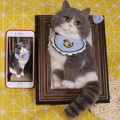 Cat wearing a blue collar with a duck design, next to a smartphone showing a similar image, on a yellow and white patterned background.