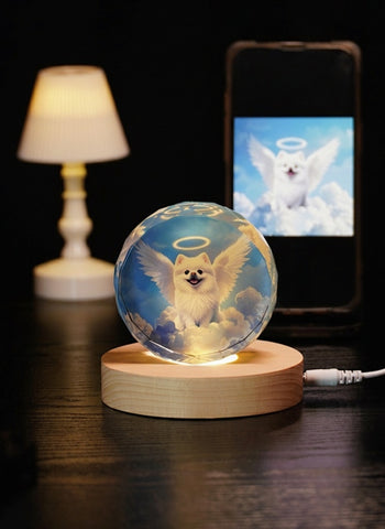 Glass ball with angel wings and a dog on a wooden base, next to a phone displaying an angelic dog image.