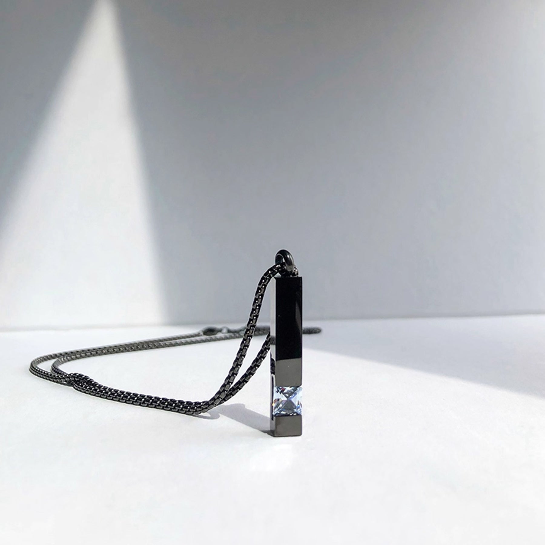 Necklace with a rectangular pendant on a white surface with a gray background