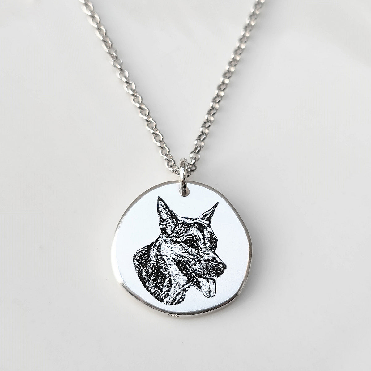 Silver necklace with a pendant featuring a black and white dog illustration on a light gray background