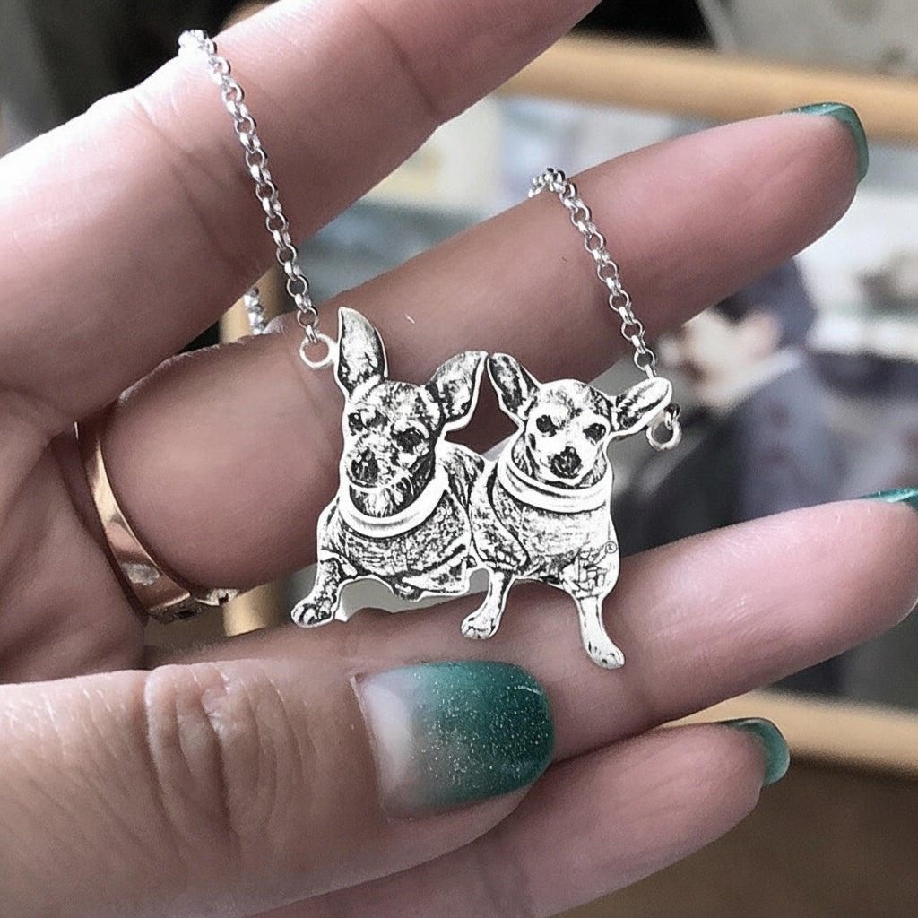 Silver pendant with two dog figures held between fingers with green nail polish.