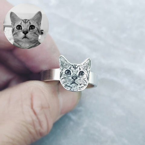 Silver cat-shaped ring on a finger with a close-up inset of a cat's face.