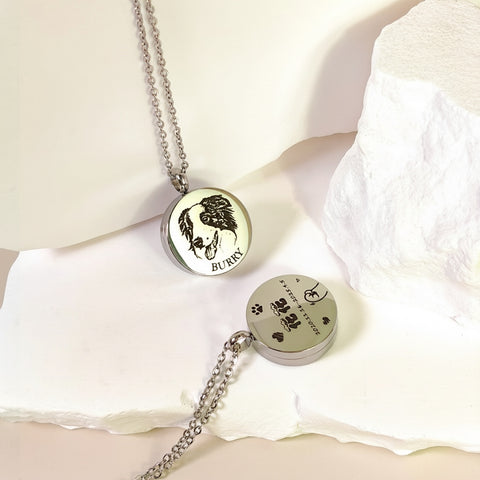 Two silver necklaces with engraved designs on a white fabric background