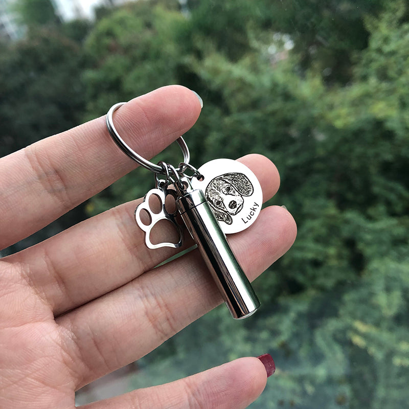 Keychain with paw print and dog tag held in a hand against a blurred green background