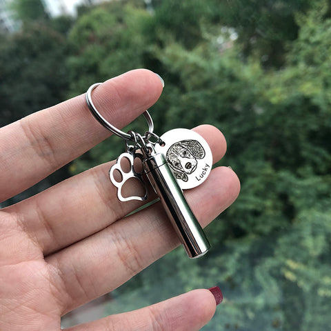 Keychain with paw print and dog tag held in a hand against a blurred green background