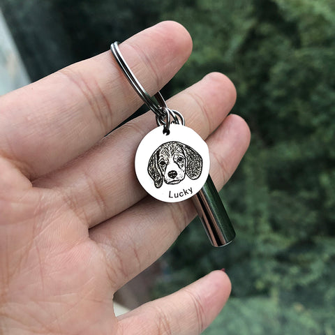 Keychain with a dog tag featuring a dog's face and the name 'Lucky' held in a hand against a blurred green background.