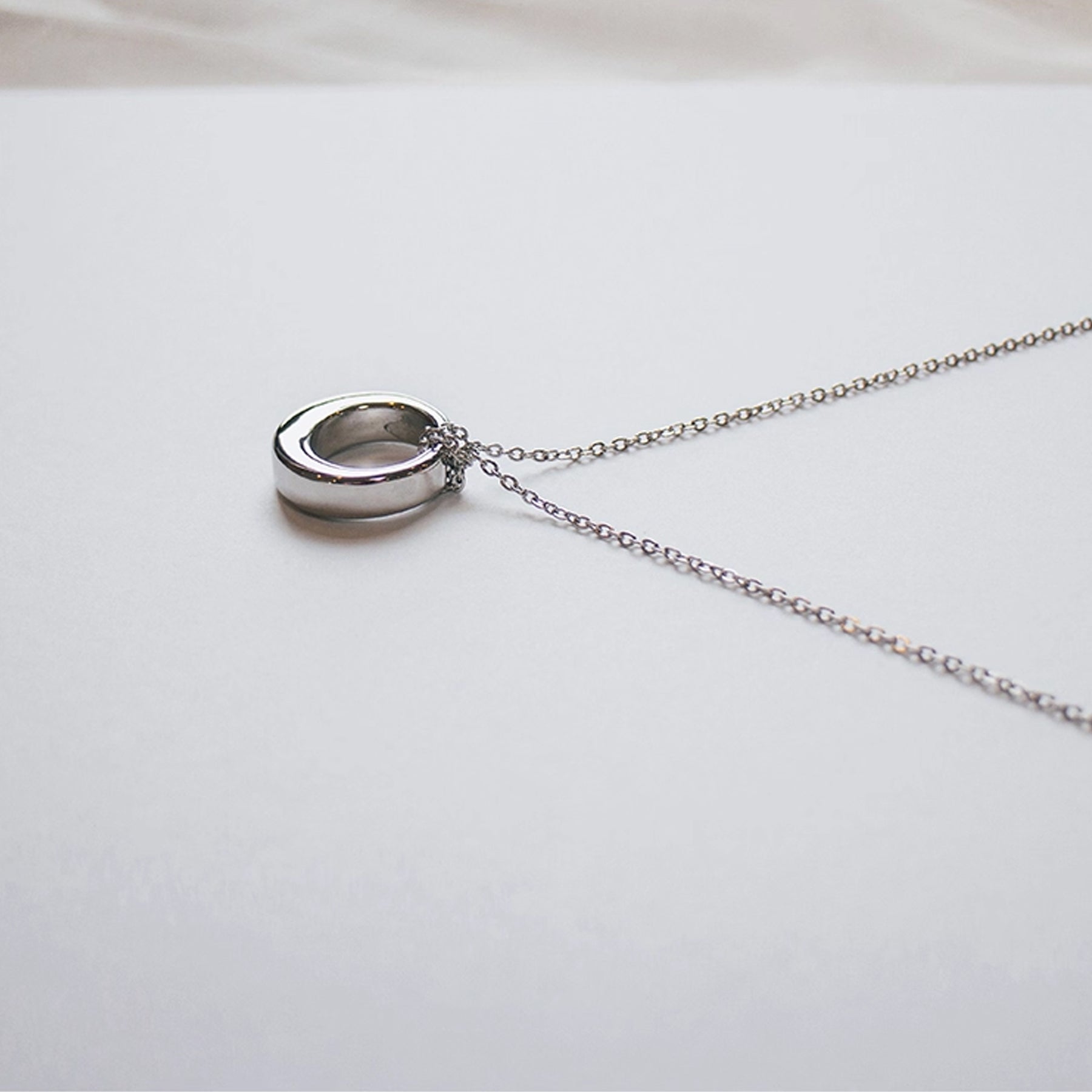 Silver necklace with a round pendant on a light gray background
