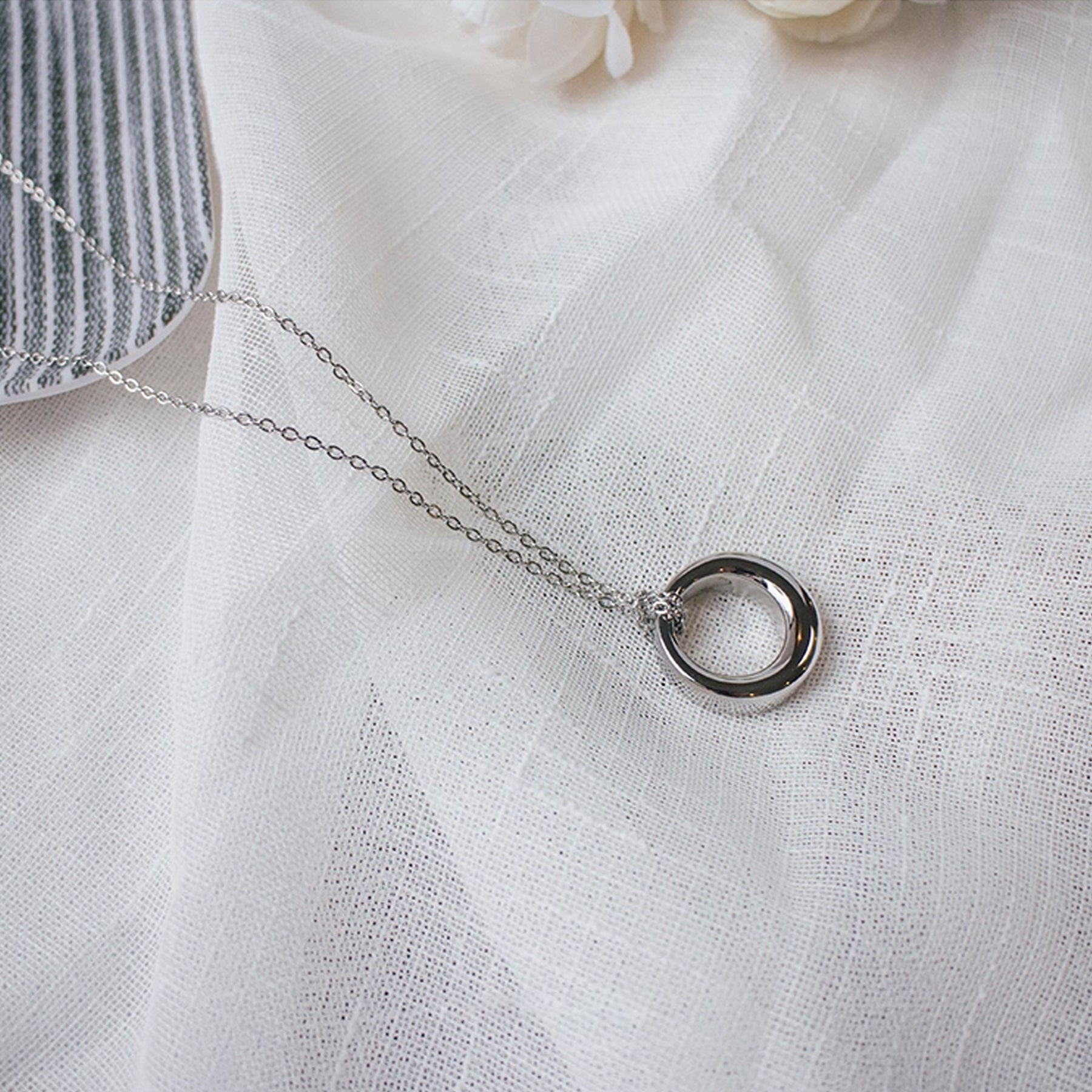Silver necklace with a circular pendant on a white fabric background