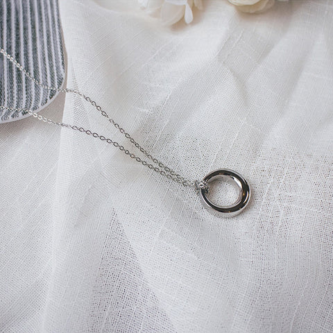 Silver necklace with a circular pendant on a white fabric background