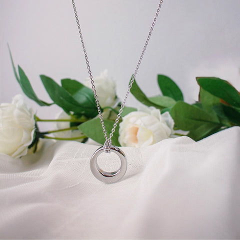Silver necklace with a circular pendant on a white surface with green leaves and flowers.