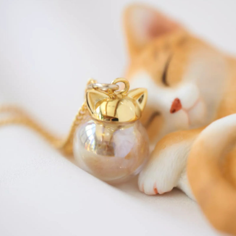 Cat-shaped keychain with gold top next to a ceramic cat figurine on a white background