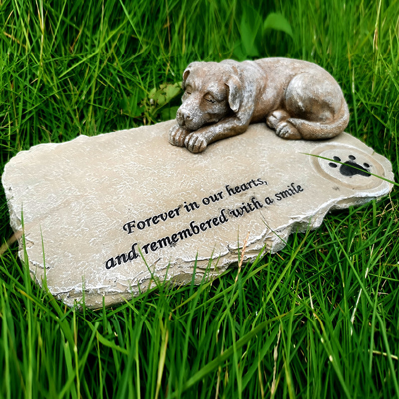 Memorial stone with a dog figurine and engraved text on grass
