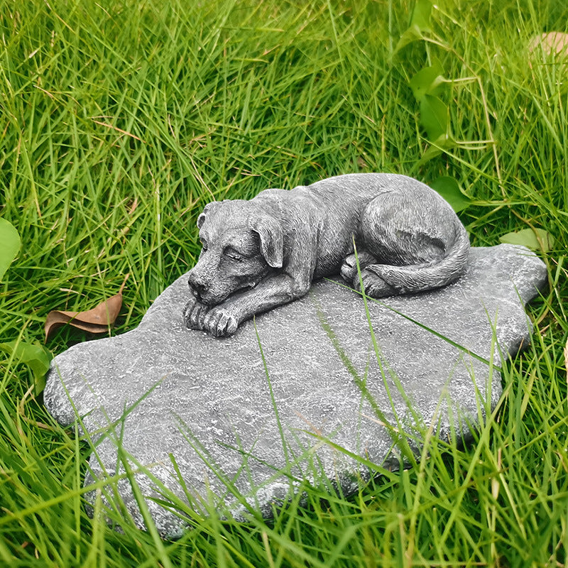 Statue of a lying dog on a rock in a grassy area