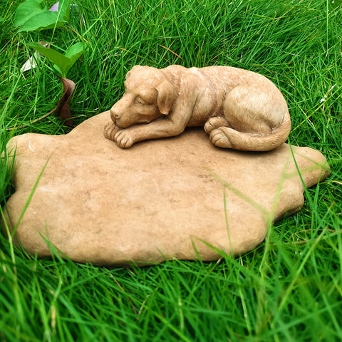 Stone sculpture of a dog lying on a rock in grass