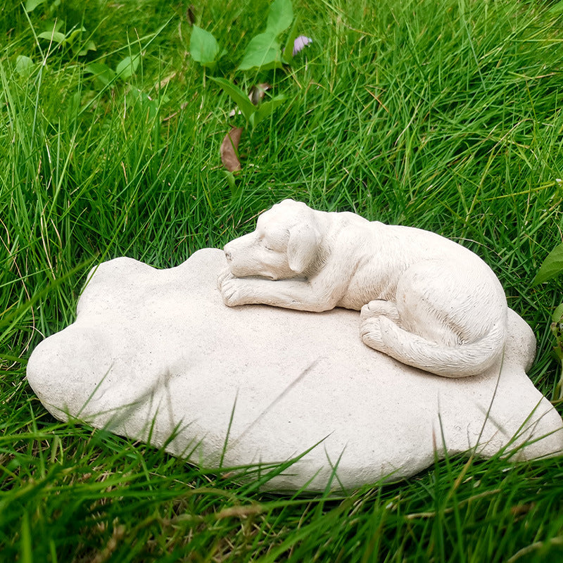 White stone sculpture of a dog lying on a rock in a grassy area