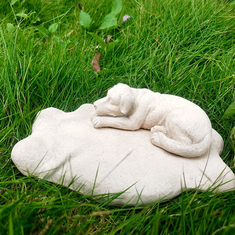 White stone sculpture of a dog lying on a rock in a grassy area