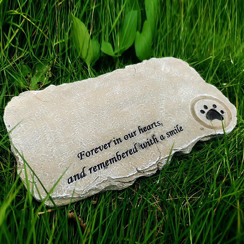 Memorial stone with paw print and text 'Forever in our hearts, and remembered with a smile' on grass.
