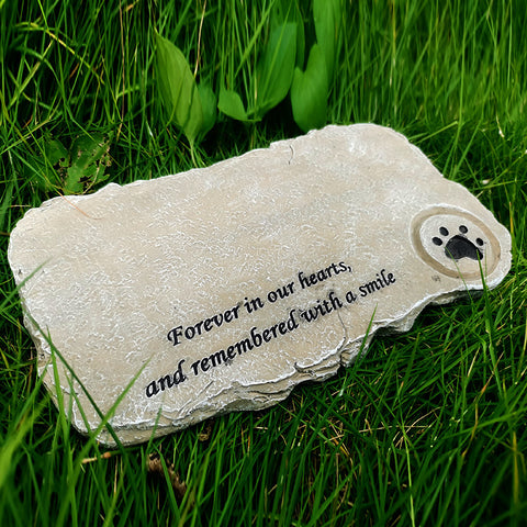 Memorial stone with paw print and text 'Forever in our hearts, and remembered with a smile' on grass.
