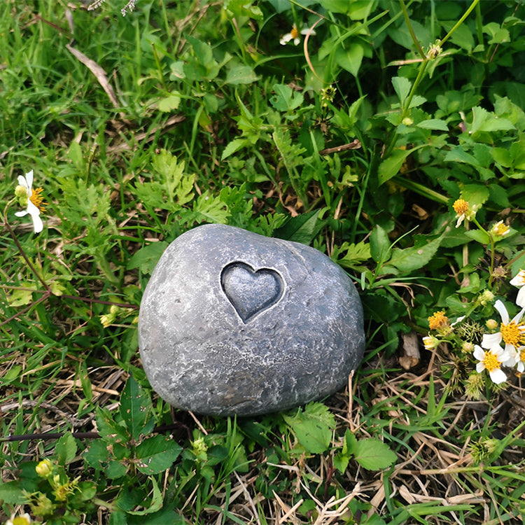 Gray stone with a heart-shaped hole in the middle on grass and flowers