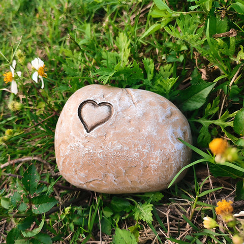 Round stone with a heart-shaped depression on grass with flowers