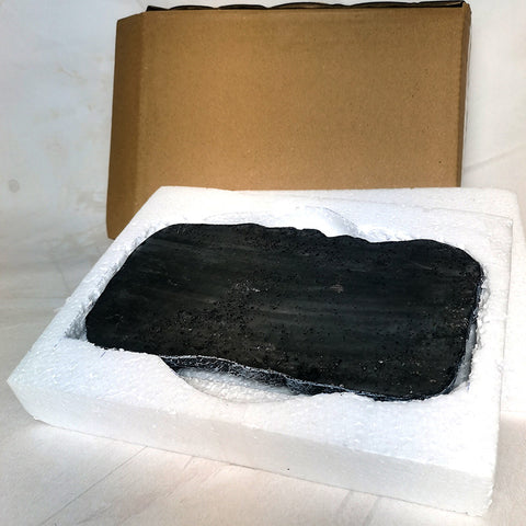 Black stone or crystal in a white foam packaging with a cardboard box in the background.