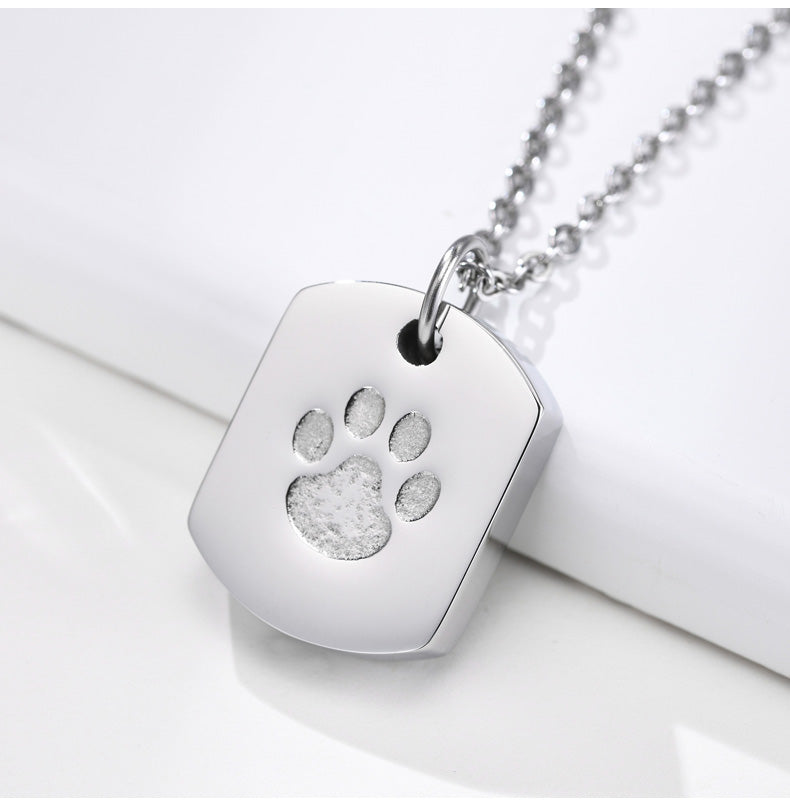 Silver necklace with a square pendant featuring a paw print on a white surface