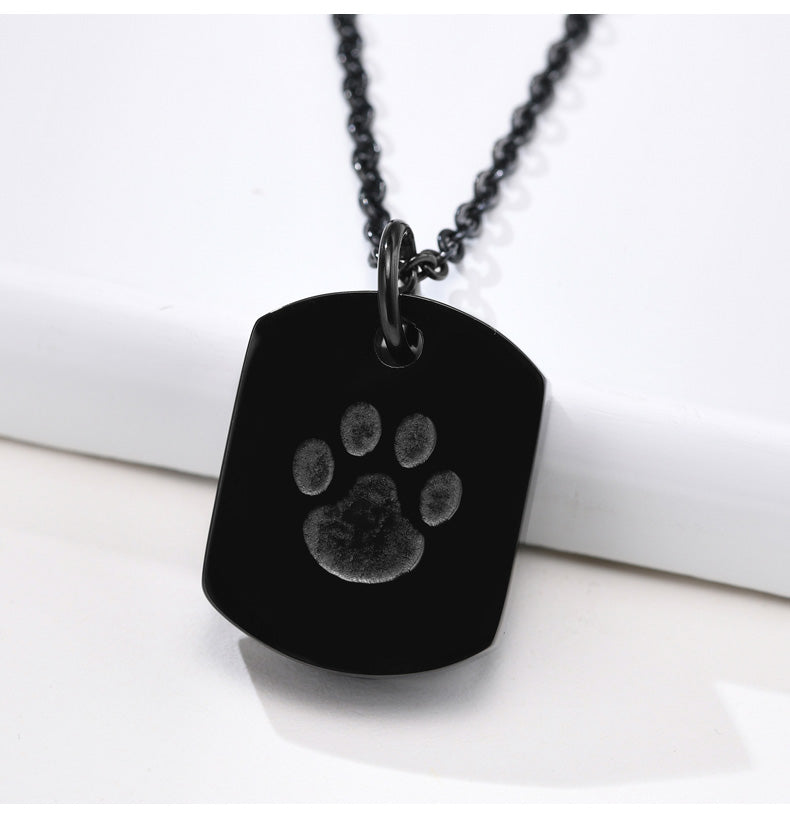 Black dog tag necklace with paw print on a white surface