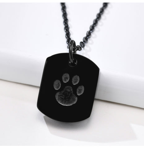 Black dog tag necklace with paw print on a white surface