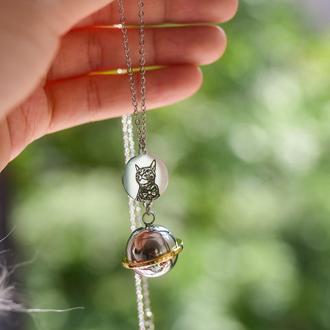 Necklace with a glass sphere pendant featuring an owl design, held by a hand against a blurred green background.