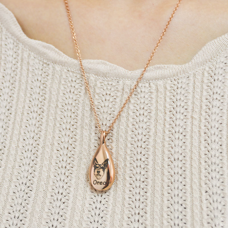 Rose gold teardrop necklace with a pendant on a person wearing a light-colored sweater.