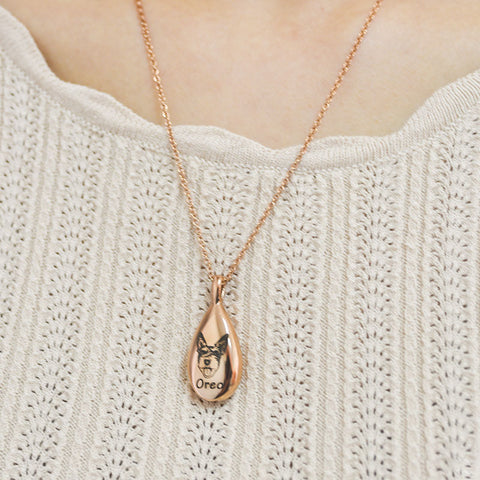 Rose gold teardrop necklace with a pendant on a person wearing a light-colored sweater.